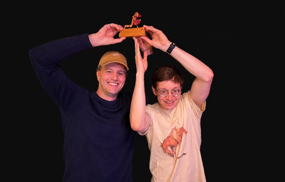 Two champions holding the golden rat trophy overhead