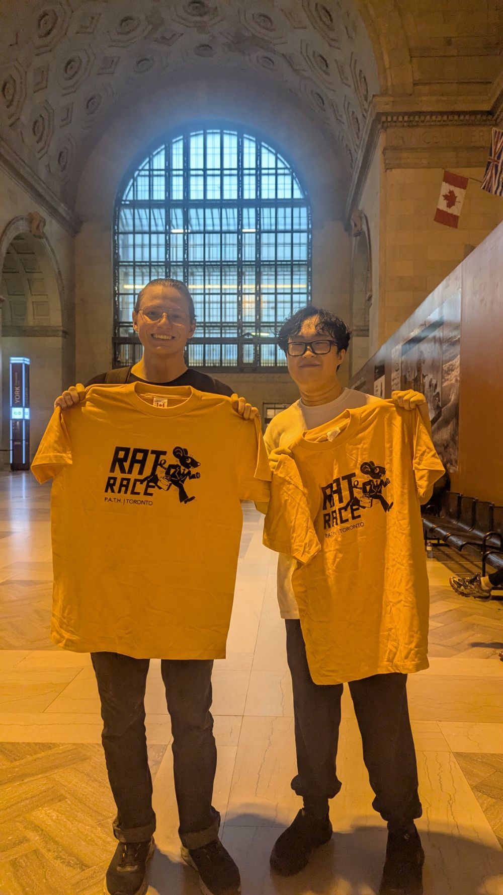 Two racers holding up their yellow Rat Race P.A.T.H. Toronto t-shirts